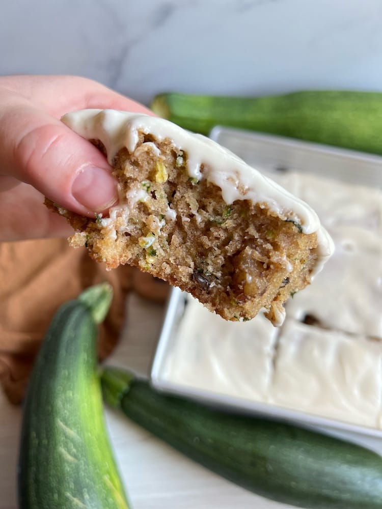 Zucchini Cake 1 A slice of Zucchini Cake held toward the camera with one bite taken out of it. Below is the pan of Zucchini Cake