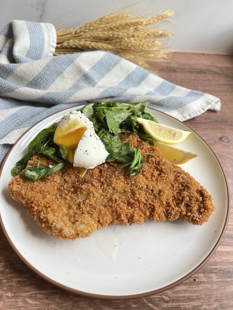 Pork Tenderloin Schnitzel 1 A Pork Tenderloin Schnitzel topped with arugula salad and a poached egg on a plate