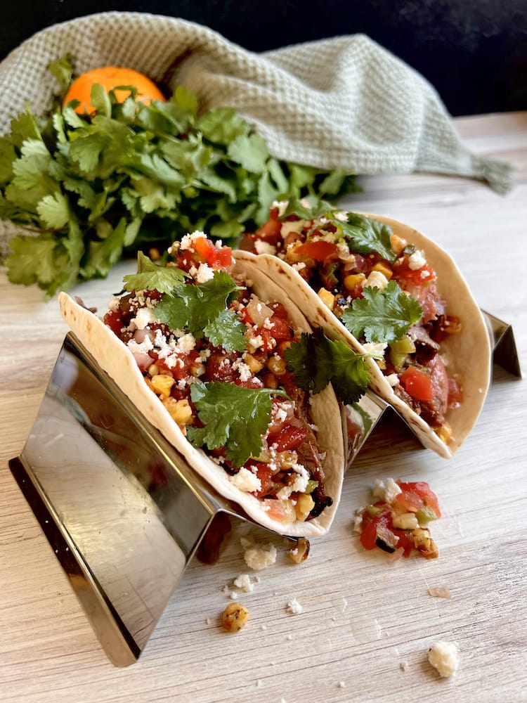 Carne Asada Tacos 2 WEB Carne Asada Tacos in a taco holder with a bunch of fresh cilantro and an orange in the background