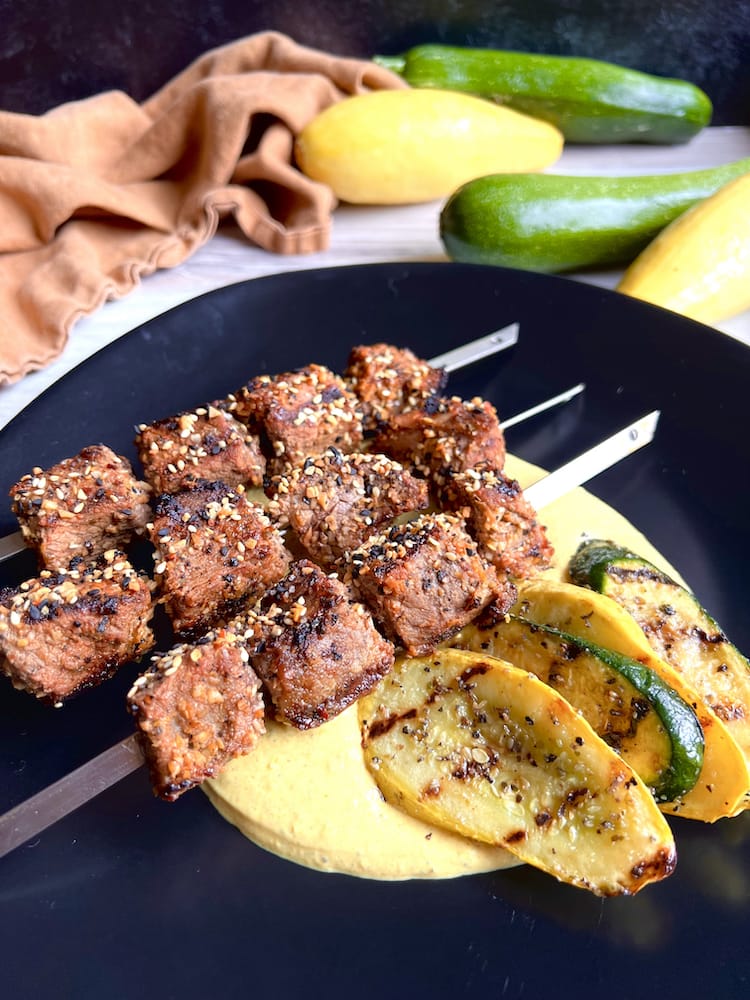 Beef Kebabs with Curried Yogurt Sauce 1 WEB Beef Kebabs with Curry Yogurt Sauce on a black plate with grilled summer squash and zucchini