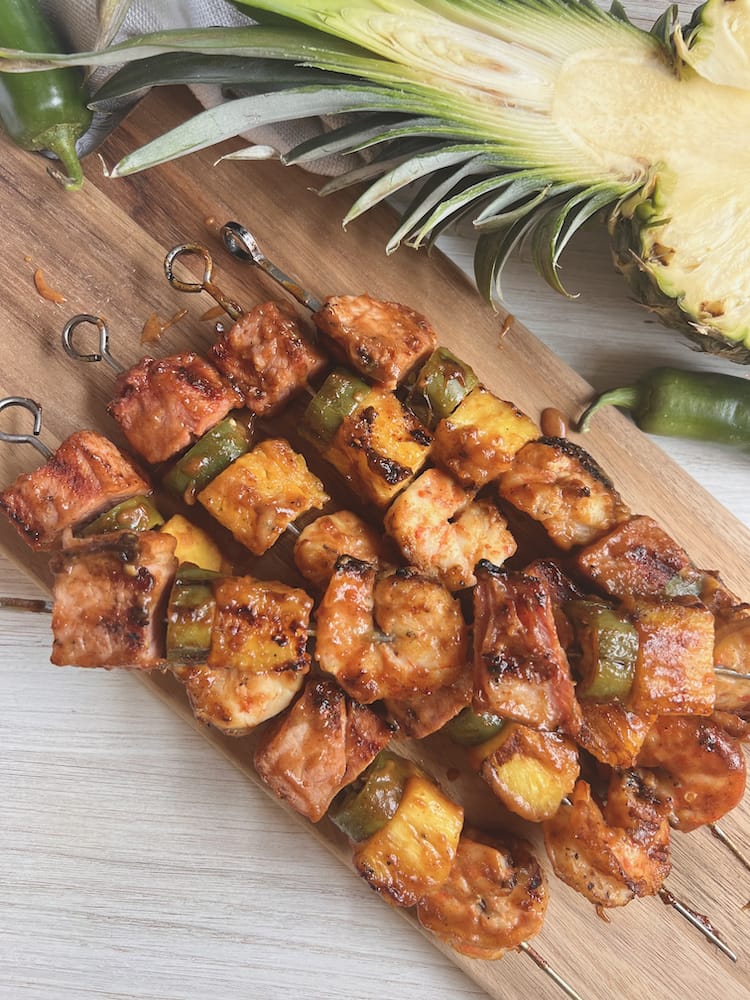 Hawaiian Ham and Shrimp Kabobs 1 WEB Hawaiian Ham and Shrimp Kabobs on a wooden cutting board with a fresh pineapple sliced in half next to them