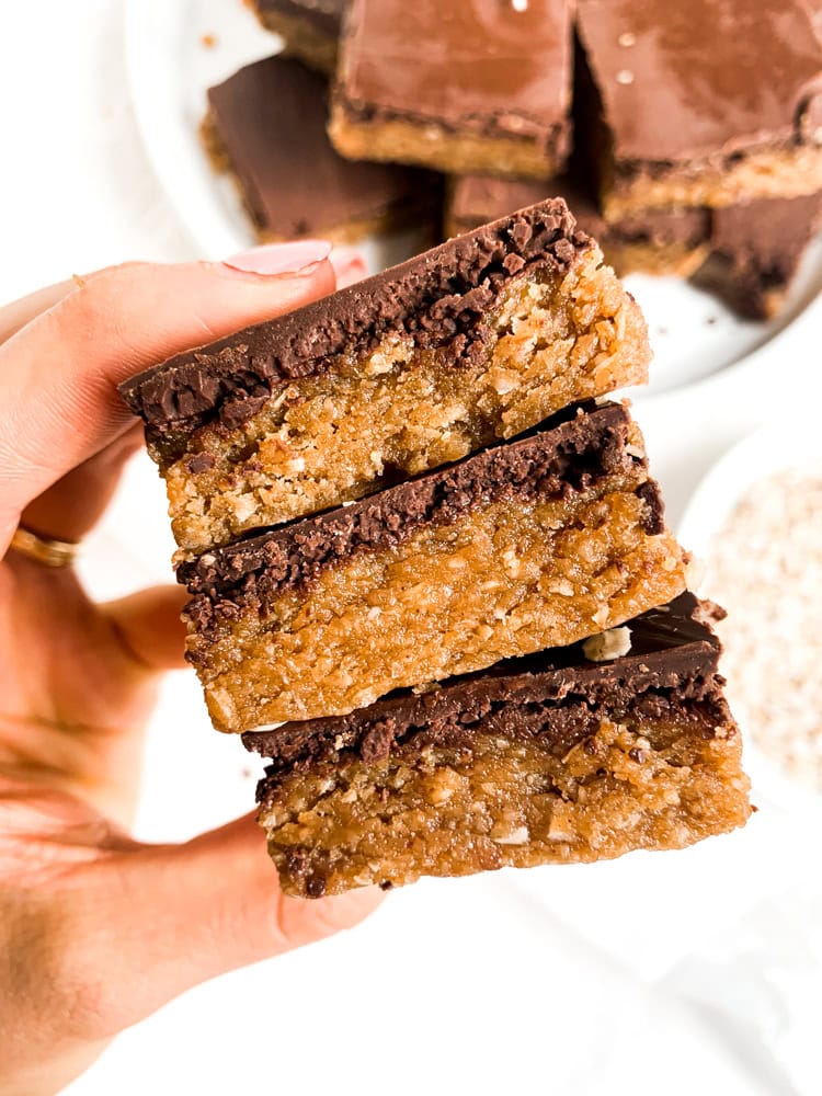 holding 3 bars above a plate of cookie dough bars on a white plate