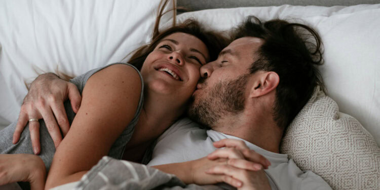 A joyful couple cuddling and smiling in bed, showcasing intimacy and emotional connection.