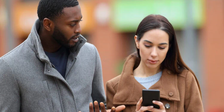 African American man and Caucasian woman looking at a smartphone outdoors, illustrating social behavior and communication in psychology studies.