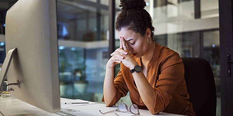 Stressed woman sitting at her desk with her head in her hands, reflecting workplace or academic pressure, mental health, anxiety, stress management, and emotional wellbeing.