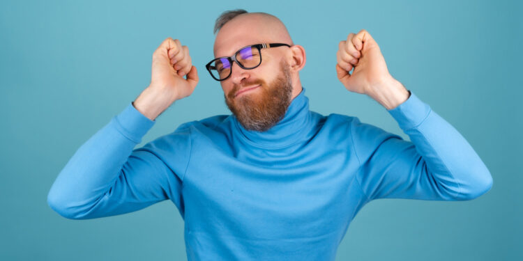 Relaxed man with glasses smiling in a blue long-sleeve shirt on colorful background, representing mental wellness and positive psychology.