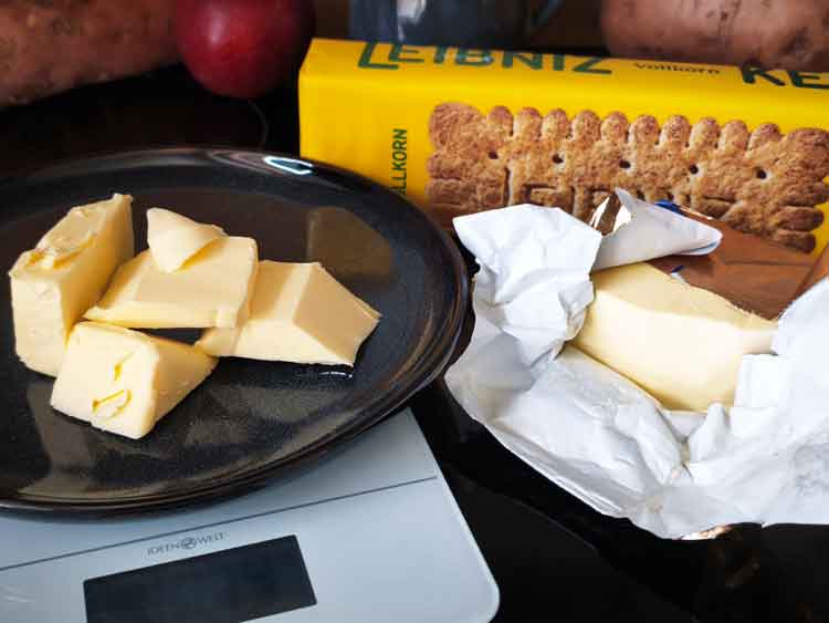 Butter liegt auf einer Küchenwage neben Vollkornkeksen.