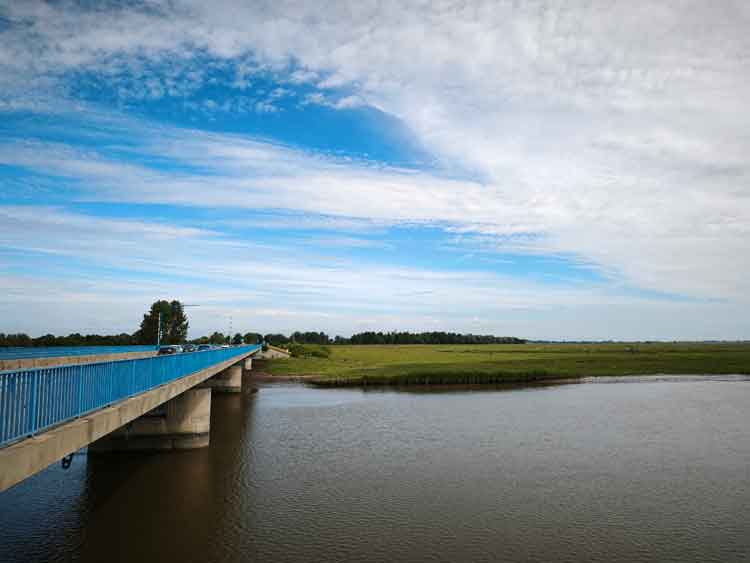 Ein Blick auf das blaue Geländer der Eider-Brücke, darunter die ruhig fließende Eide