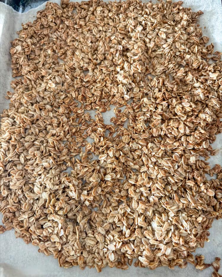 Close up of cooked homemade granola on top of brown parchment paper on top of a stainless steel cookie sheet.