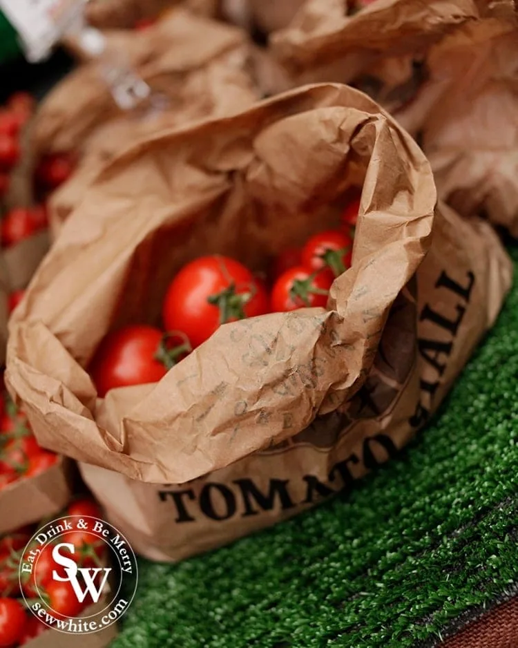 A brown paper bag of tomatoes on the market stall.