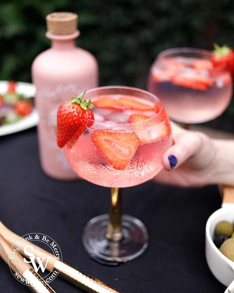 Hand holding the strawberry gin and tonic. Condensation on the glass and a strawberry as decoration. 