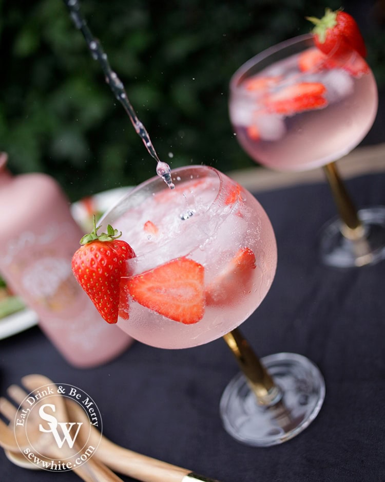 Fever tree tonic being poured in to the gin balloon glass with strawberries inside.