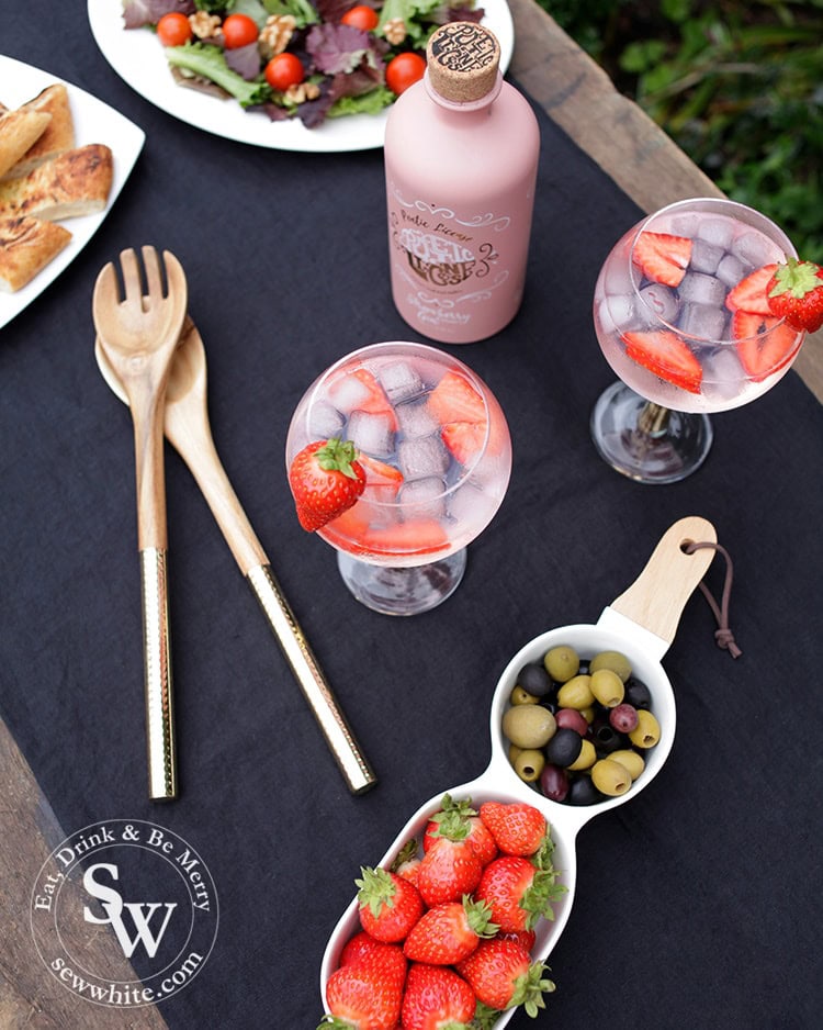 Table setting for a wimbledon party with navy blue table cloth, gin glasses with strawberries in and strawberries and olives on display.