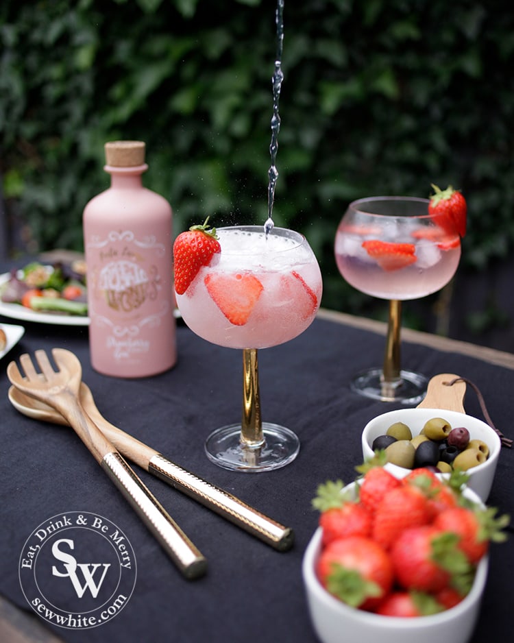 Tonic water being poured into a strawberry gin and tonic on a blue table.