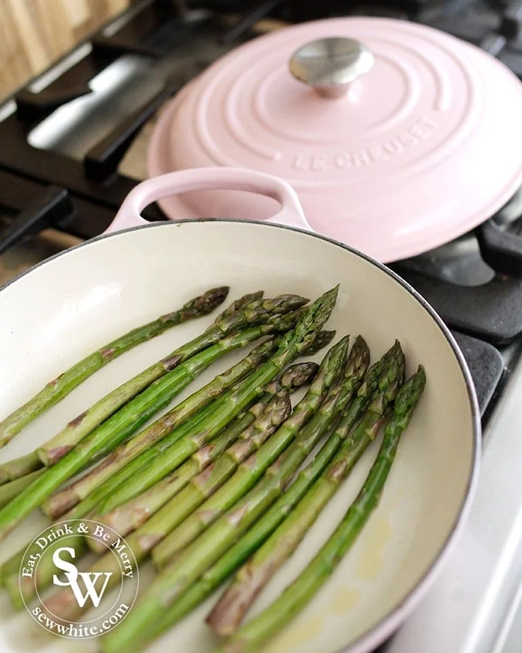 Asparagus cooking in a pink le creuset shallow casserole dish 