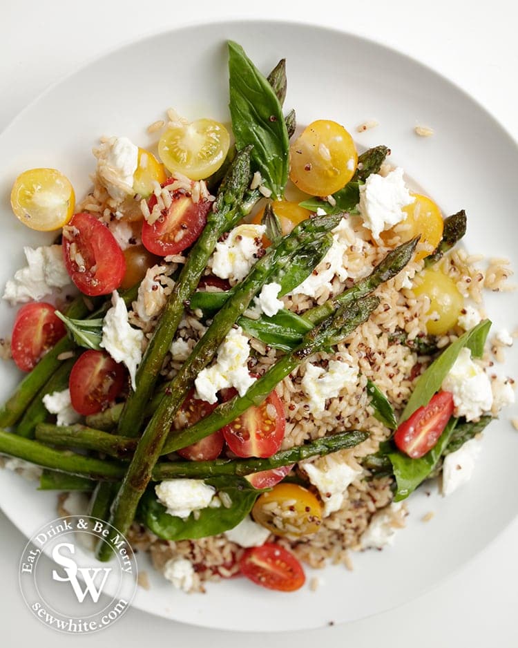 Asparagus placed on top of a bed of rice, mozzarella and tomatoes.