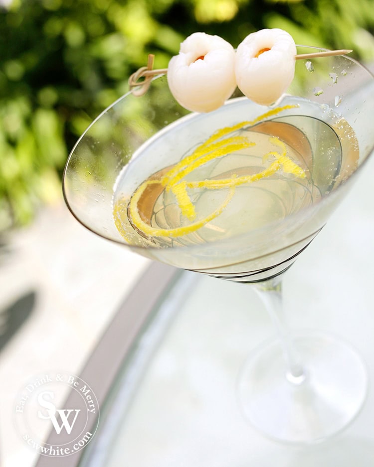 Freshly served up Lemon Lychee Martini in a large glass martini glass with strips of lemon inside and decorated with lychees. 