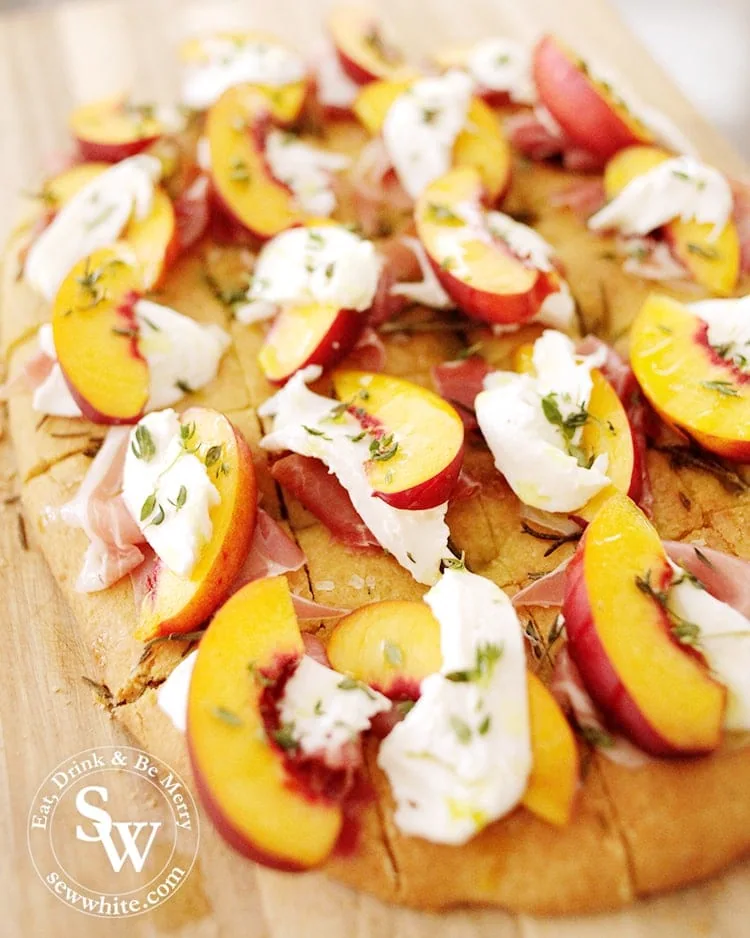 Homemade golden Focaccia cut up into pieces topped up with parma ham, peach slices, mozzarella and decorated with thyme and drizzled with olive oil. Easy Party Bites.