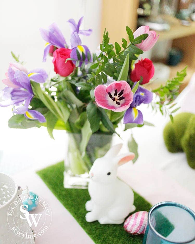 the cutest rabbit statue  on fake green grass and with fresh tulips, irises, roses and greenery