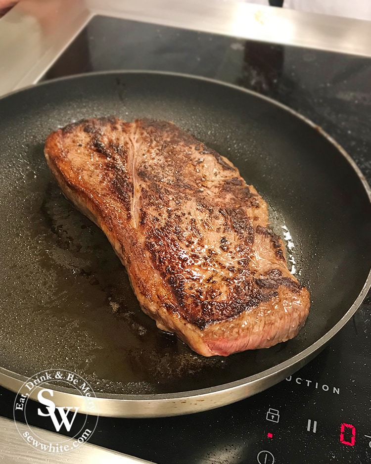 Large piece of sirloin steak being cooked in a pan.