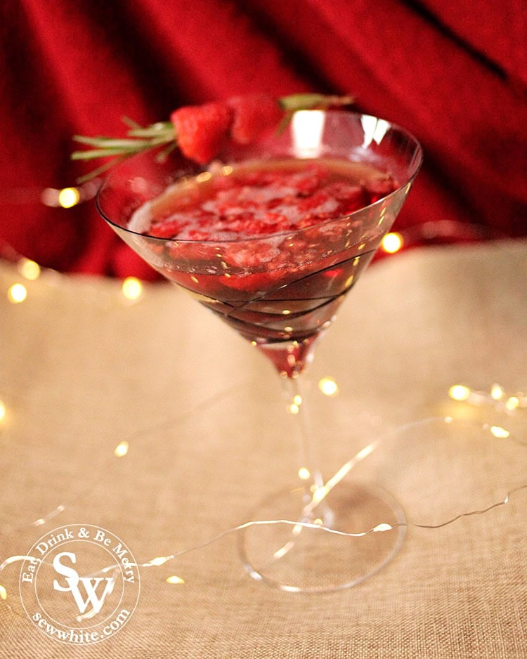 A dark deep red raspberry cocktail served with a sprig of rosemary and fresh raspberries