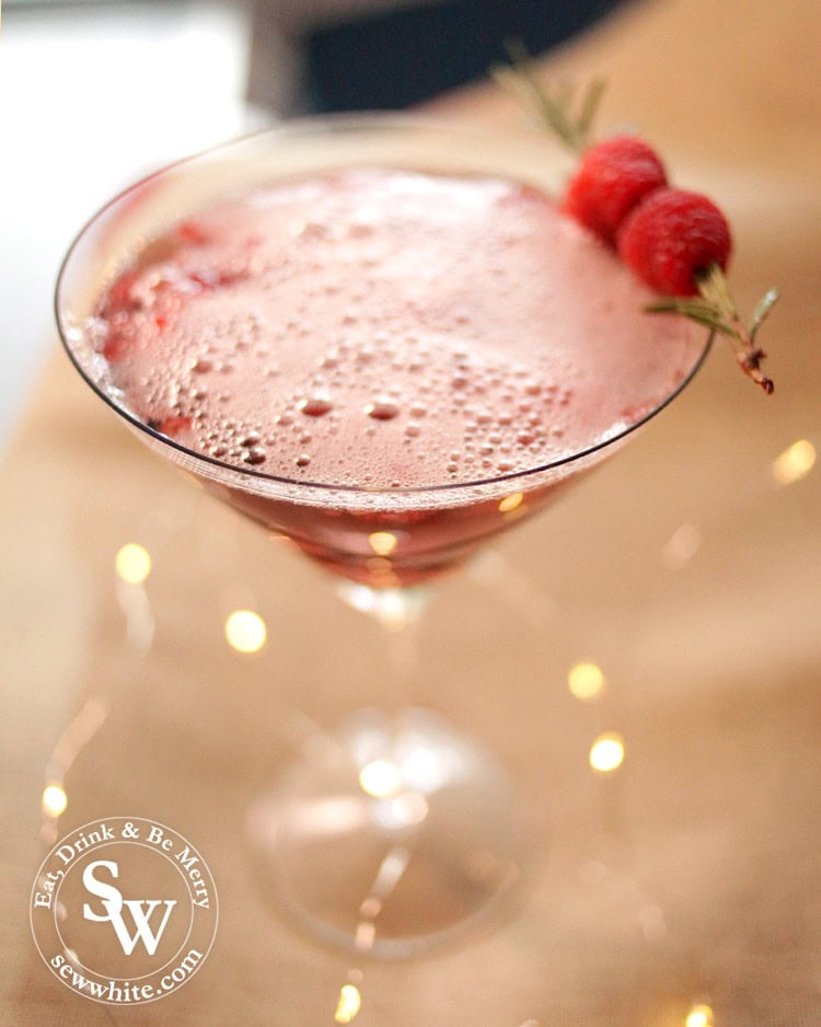 Red and fizzy Christmas Rum and Raspberry Cocktail topped with rosemary and fresh raspberries. 