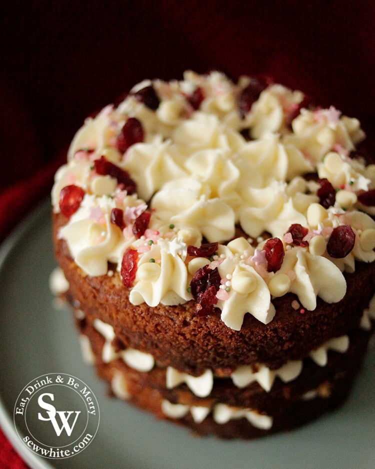 Three tiered golden brown white chocolate cranberry cake decorated with buttercream swirls, dried cranberries and white chocolate chips. Plus pink star sprinkles.