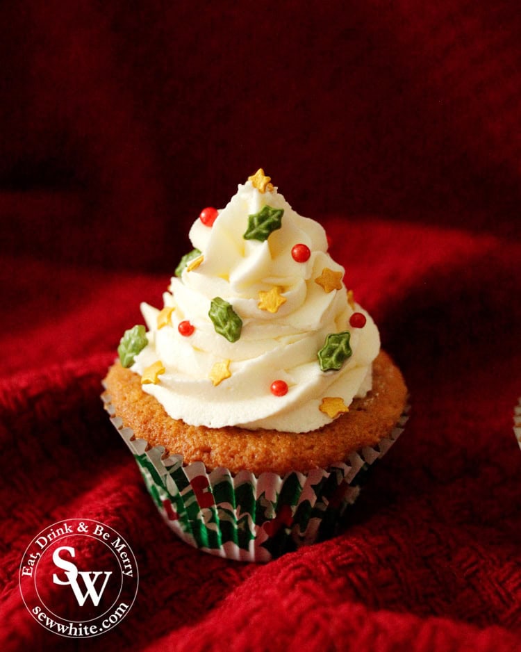 Elegant Christmas cupcakes decorated with little holly leaf sprinkles, red sprinkles and gold stars.