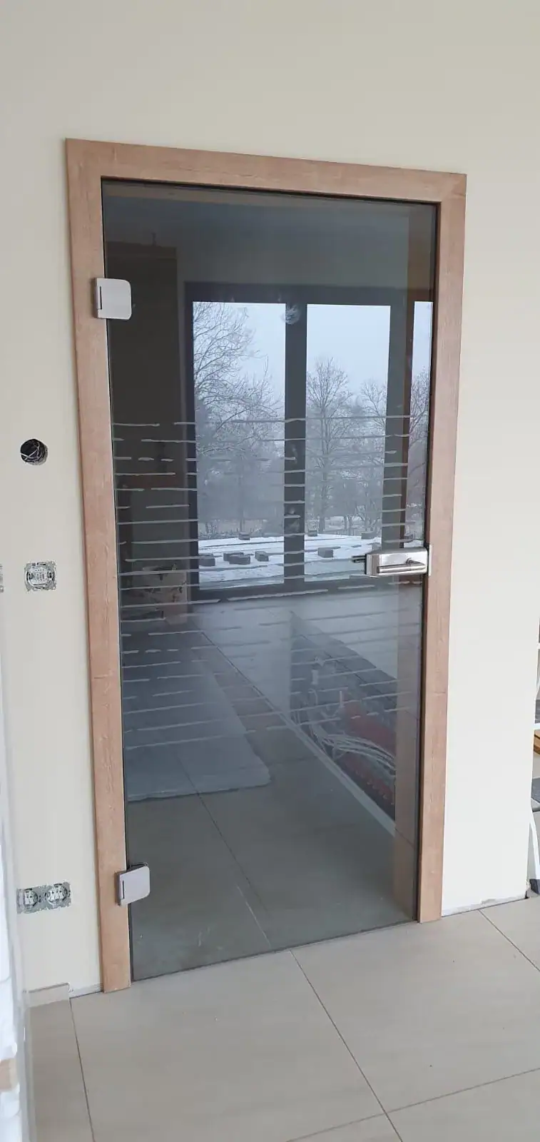Moderne Glastür mit hellem Holzrahmen und horizontalen, satinierten Streifen im Glas, inklusive silberfarbenen Beschlägen. Eine stilvolle Zimmertür von Fütterer Fenster & Türen GmbH.