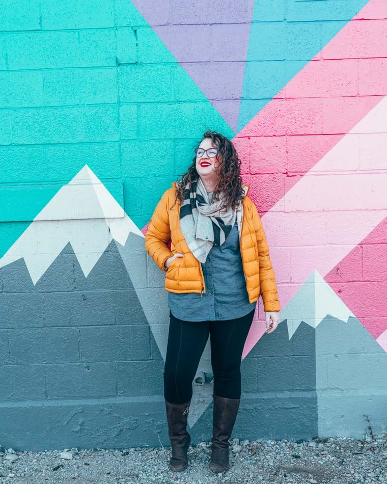 Lia in a down jacket in front of a mountainy street mural in Salt Lake City, Utah.