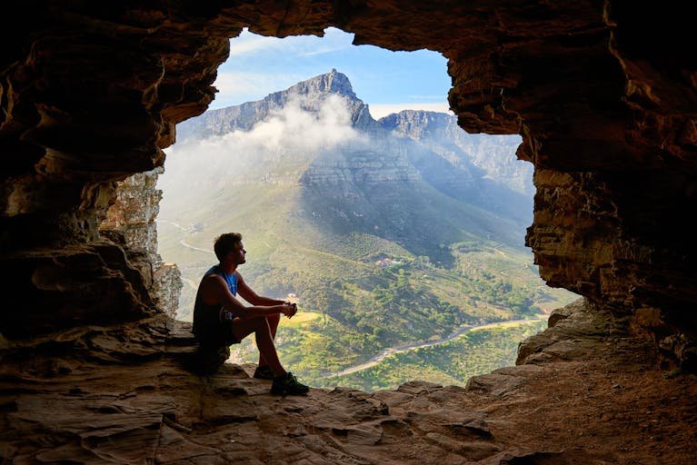 A solitary man sitting in the entrance of a desert cave in contemplation