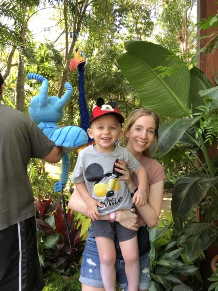 Blue snail puppet, lush tropical greenery, woman and child enjoying a jungle-themed adventure.