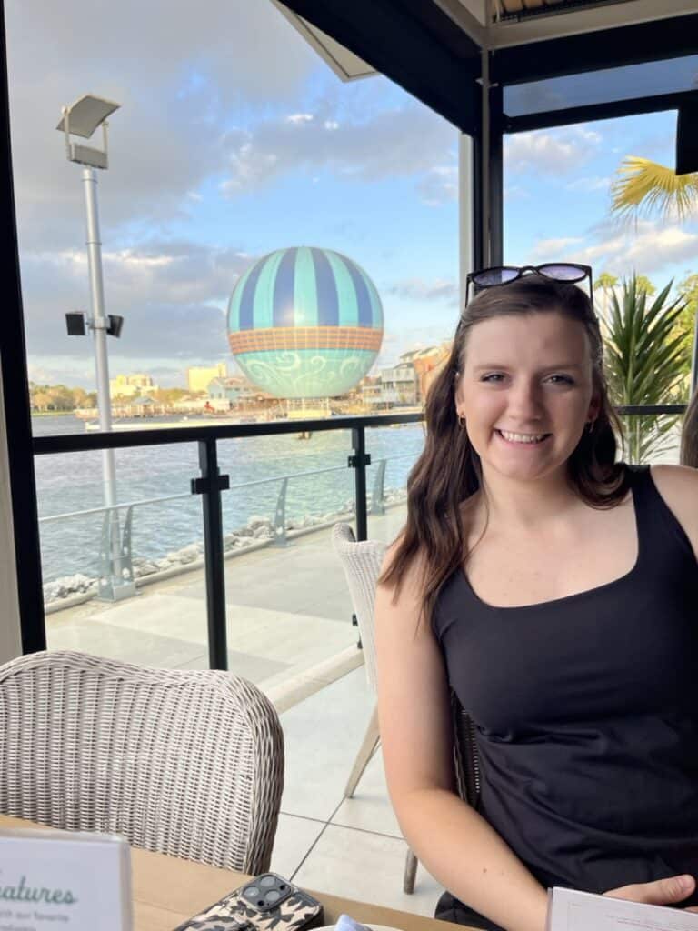 Vibrant woman enjoying waterfront view with hot air balloon in background, outdoor dining at 407 and Beyond Vacation Co.