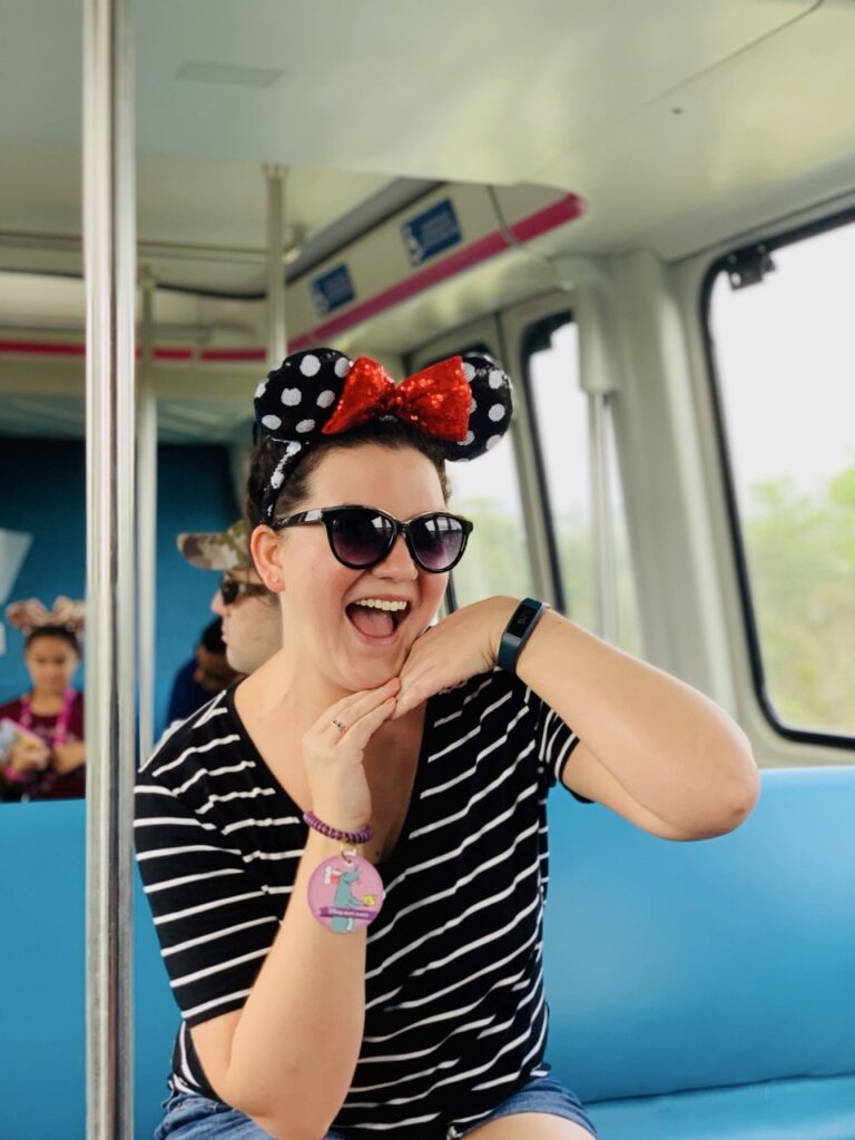 Fun woman wearing Minnie Mouse ears and sunglasses on a Disney transportation ride, enjoying a vacation.