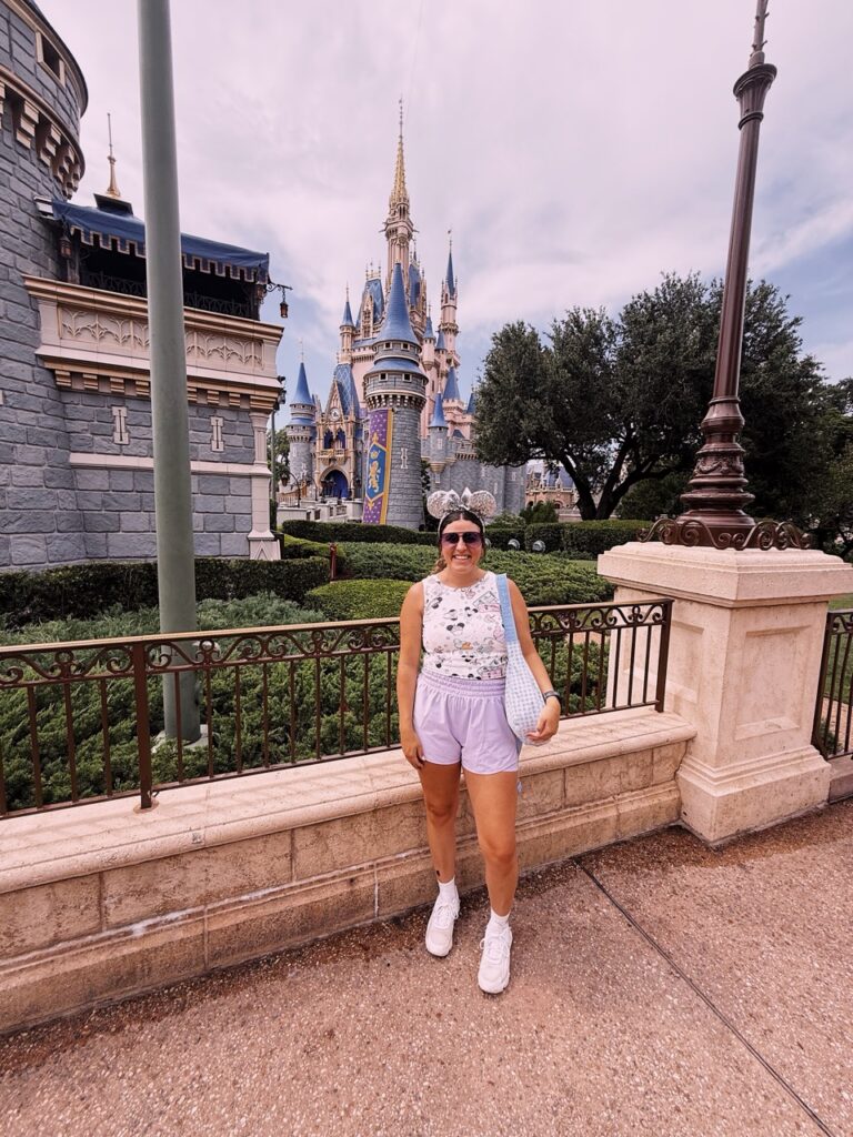Enchanting Disney castle with a smiling woman in front, experiencing a magical vacation at Disneyland.