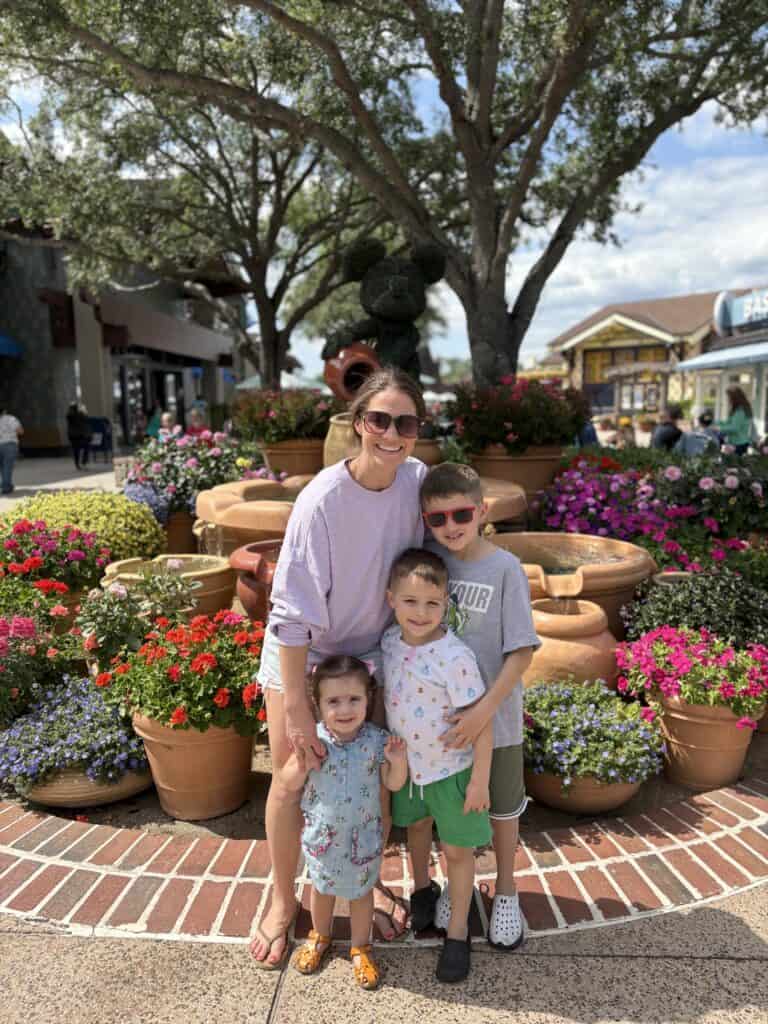 Family exploring a lively outdoor shopping district with blooming flowers and shaded trees.