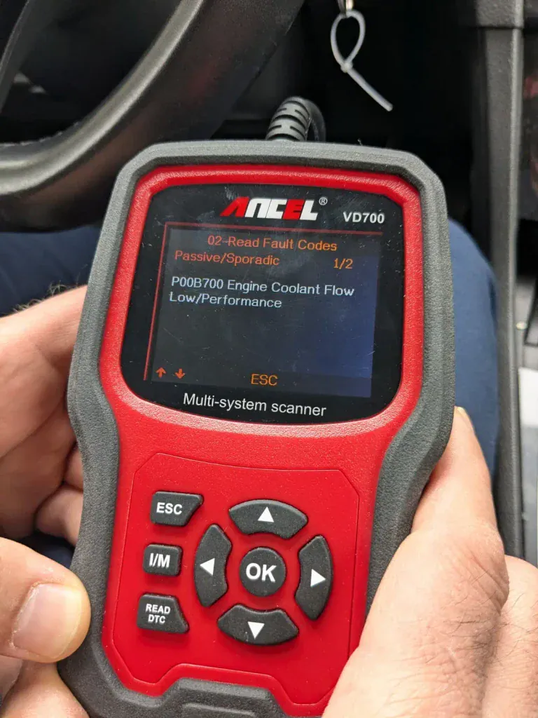 Close-up of a red and black ANCEL VD700 multi-system OBD scanner held in a car, screen displaying fault code P00B700 Engine Coolant Flow Low/Performance, 1 of 2 codes.