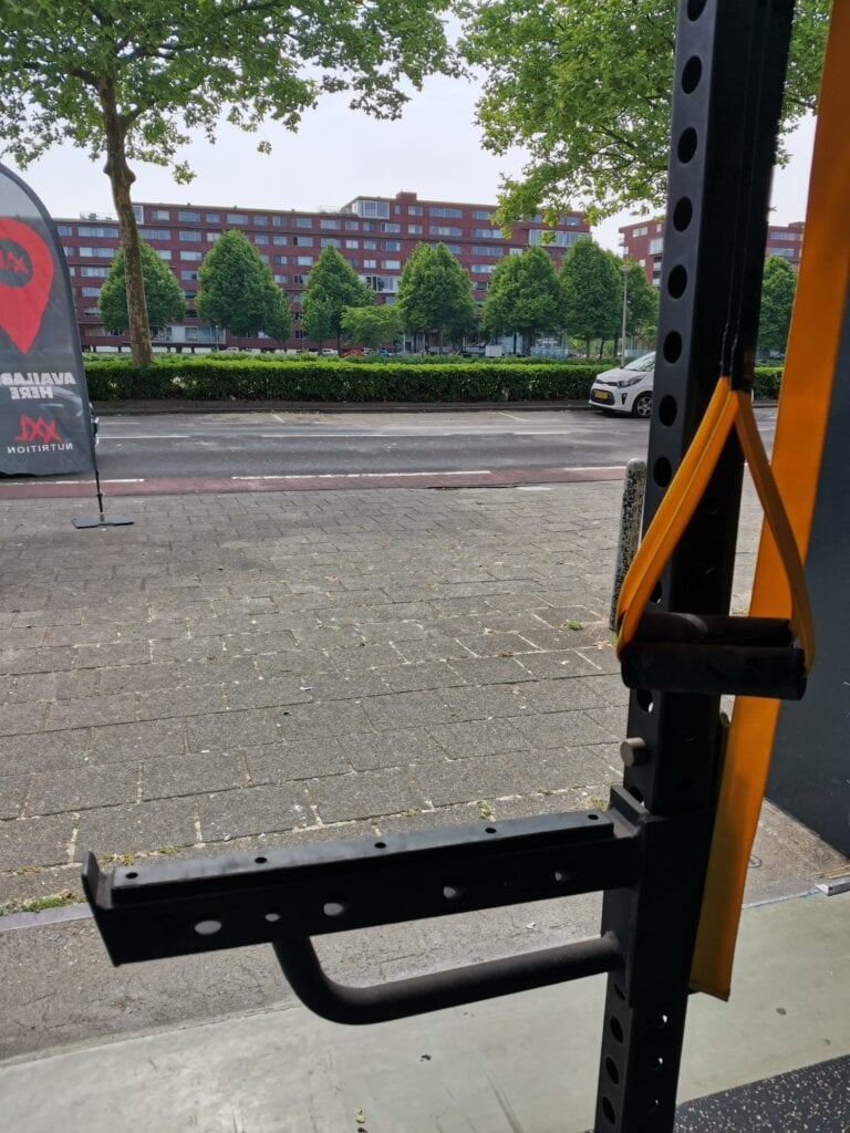 Uitzicht naar buiten vanuit de gym, met een robuust crossfit rack bij de ingang, klaar voor krachttraining en functionele oefeningen