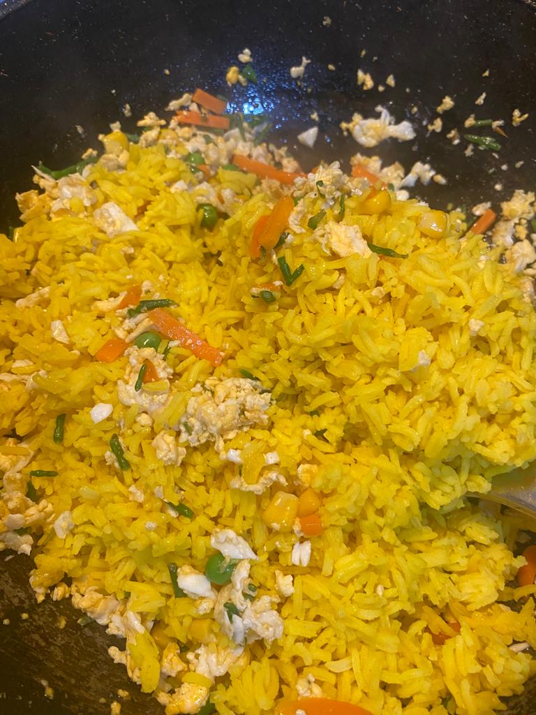 Turmeric rice being stirred into a colorful mix of scrambled eggs and vegetables