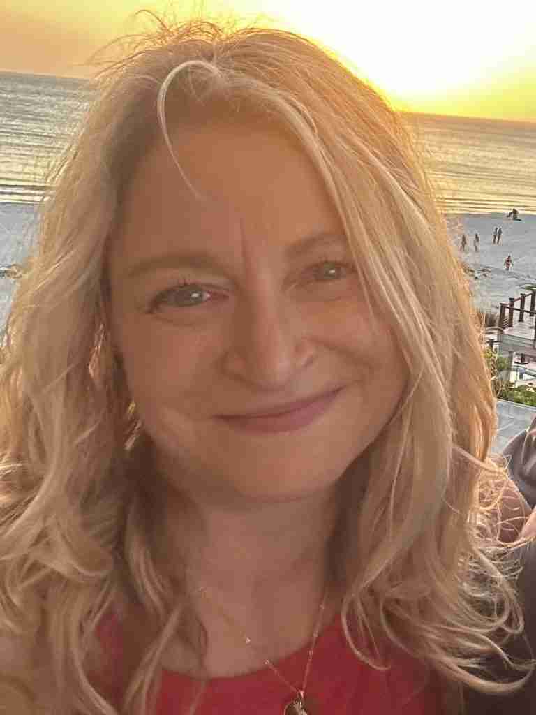Close-up of a smiling woman with blonde hair at the beach during sunset, ocean in the background