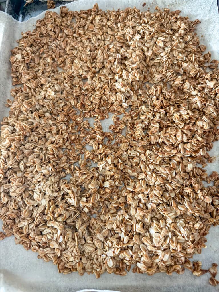 Close up of cooked homemade granola on top of brown parchment paper on top of a stainless steel cookie sheet.