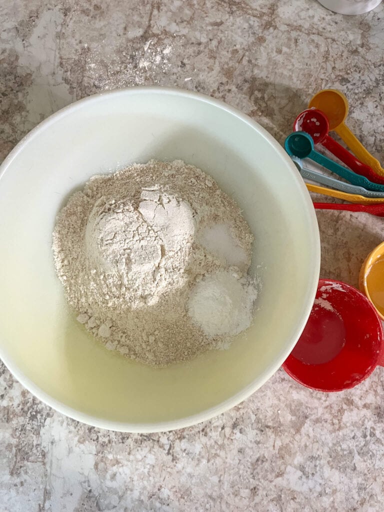 Dry ingredients for blueberry muffins in a ceramic bowl with measuring utensils next to it.