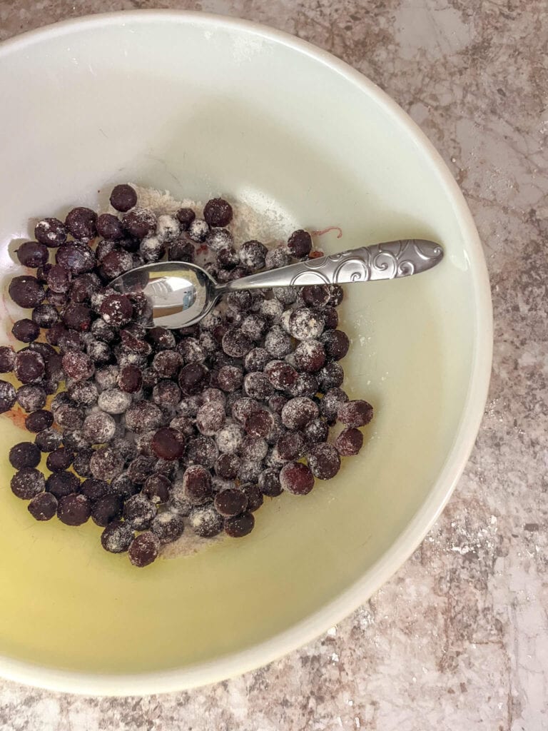 Frozen blueberries mixed with flour in a large ceramic bowl with a silver spoon.