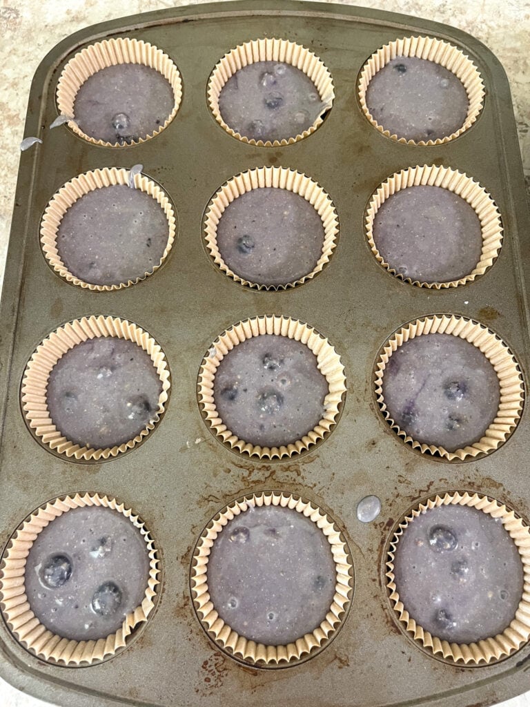 Unbaked blueberry muffin batter in cupcake liners in a baking tin.