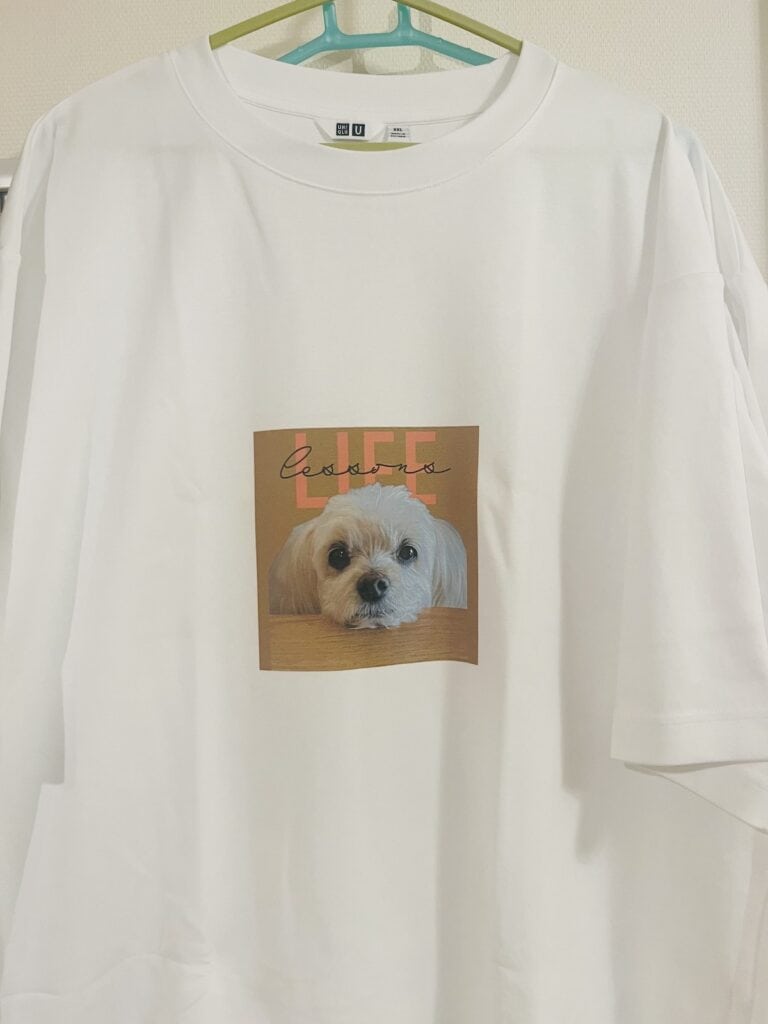 愛犬の写真とロゴがプリントされた白いTシャツ。ハンガーにかけられている