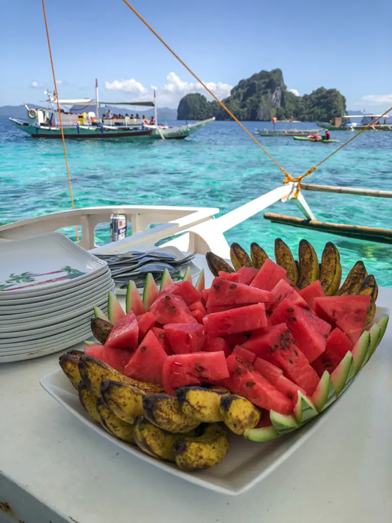 A picture of a some snacks on a small boat used for island hopping in the Philippines.  There are several other boats in the picture as well.
