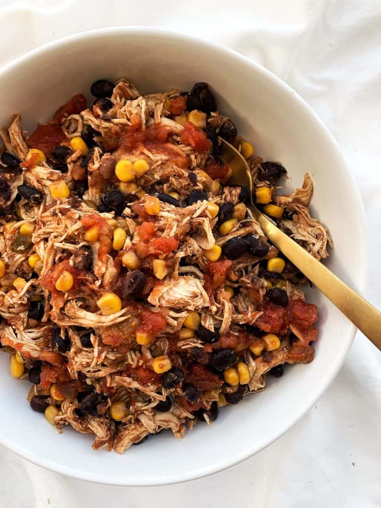 Overhead shot of slow cooker tex mex chicken with corn, black beans, chicken, salsa, and a gold spoon