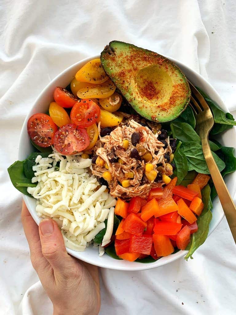 White bowl with Crockpot Tex Mex Chicken, bell peppers, shredded cheese, tomatoes, and spinach