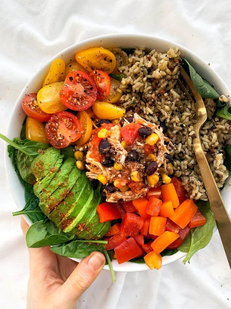 Overhead shot of crockpot tex mex chicken with brown rice, diced belle pepper, sliced avocaod, and cherry tomatoes over lettuce