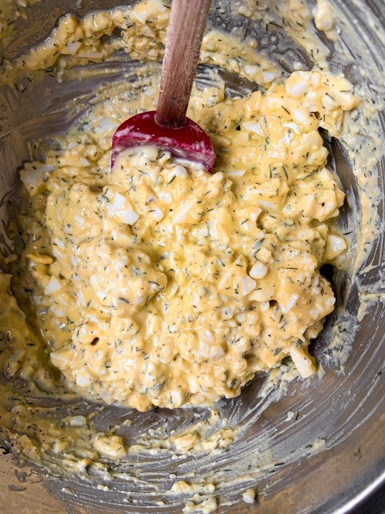 all of the ingredients for healthy egg salad in a mixing bowl with spatula